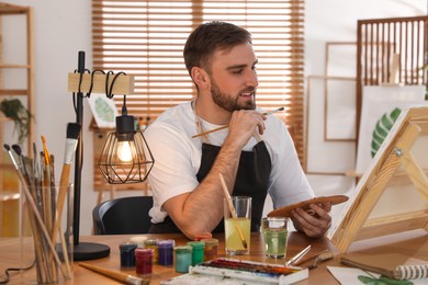 Photo of Young man painting on easel with brush in artist studio