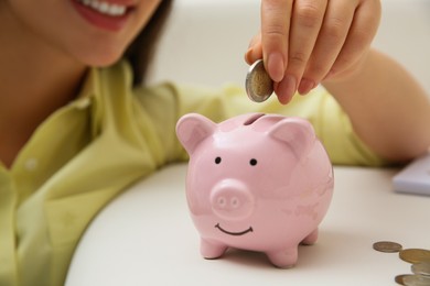 Photo of Woman putting coin into piggy bank indoors, closeup. Money savings