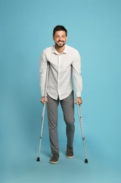 Full length portrait of man with crutches on light blue background
