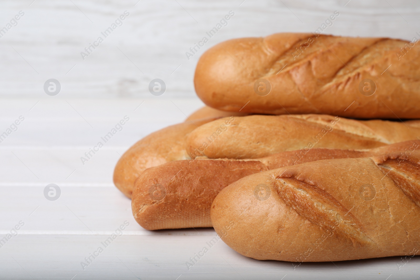 Photo of Tasty baguettes on white wooden table, closeup. Space for text