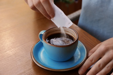 Woman adding sugar to fresh aromatic coffee at table, closeup