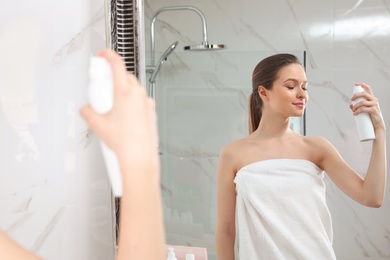 Young woman applying thermal water on face near mirror in bathroom. Cosmetic product