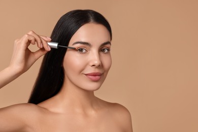 Photo of Beautiful woman applying serum onto her eyelashes on beige background, space for text. Cosmetic product