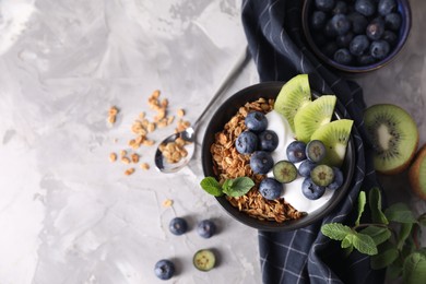 Photo of Tasty granola with yogurt, blueberries and kiwi in bowl on gray textured table, flat lay. Space for text