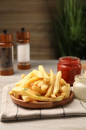 Delicious french fries served with sauces on light wooden table