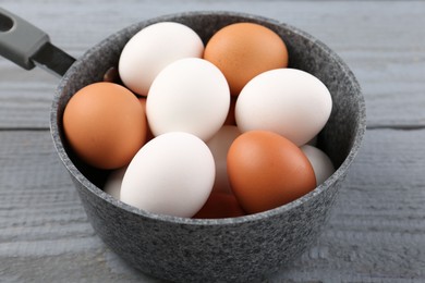 Unpeeled boiled eggs in saucepan on grey wooden table, closeup