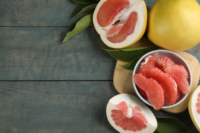 Photo of Fresh cut and whole pomelo fruits with leaves on blue wooden table, flat lay. Space for text