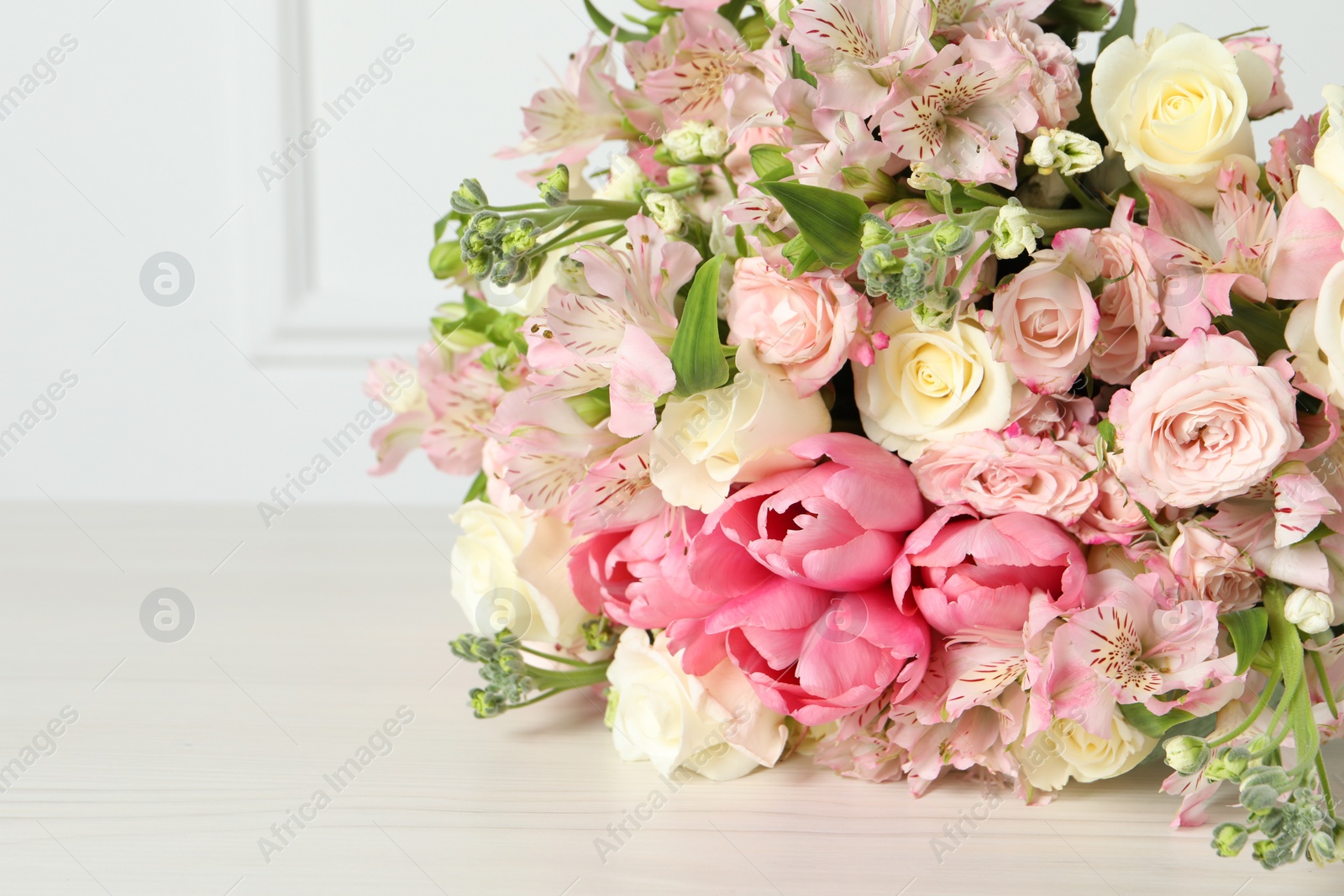 Photo of Beautiful bouquet of fresh flowers on table near white wall, closeup