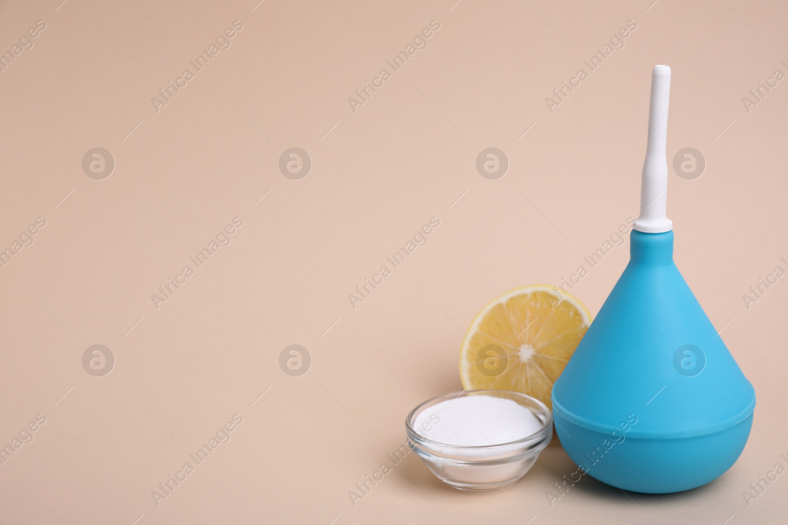 Photo of Enema, lemon and bowl of salt on beige background, space for text. Medical treatment