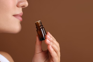 Woman with bottle of essential oil on brown background, closeup. Space for text