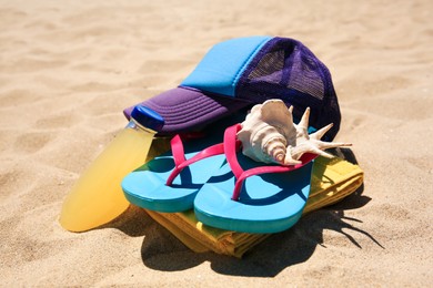 Photo of Cap, flip flops, seashell and refreshing drink on beach, closeup