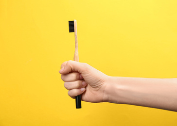 Photo of Woman holding bamboo toothbrush on yellow background, closeup