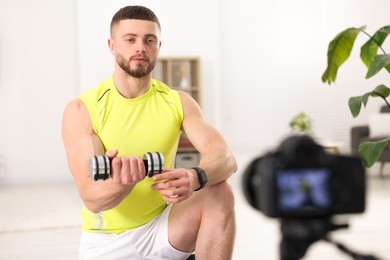 Photo of Trainer with dumbbell recording workout on camera at home