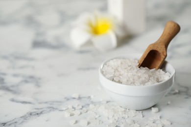 Sea salt and wooden scoop on white marble table, space for text