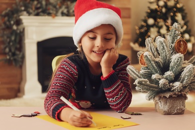Cute child writing letter to Santa Claus at table indoors. Christmas tradition