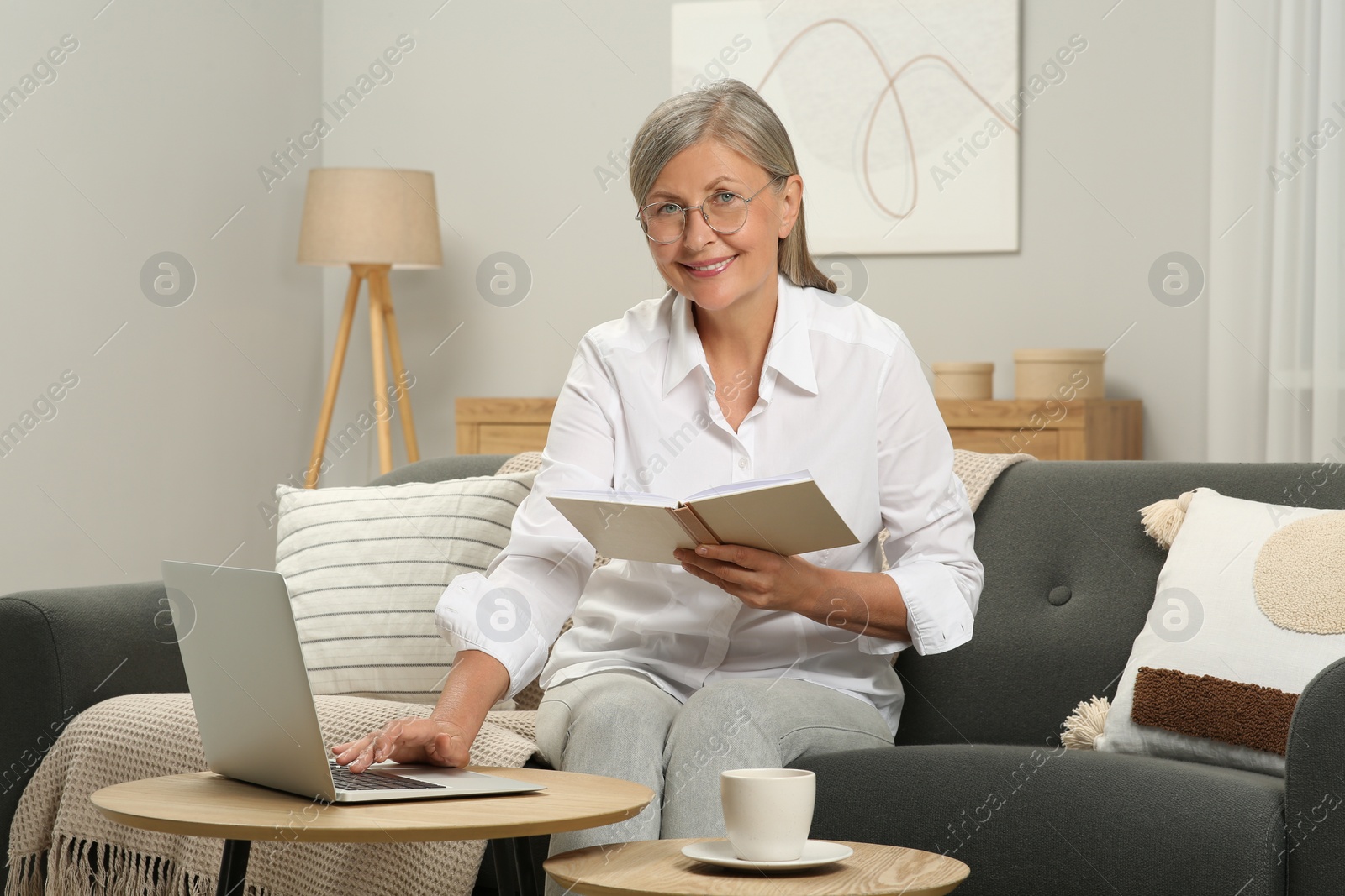 Photo of Beautiful senior woman with notebook using laptop at home