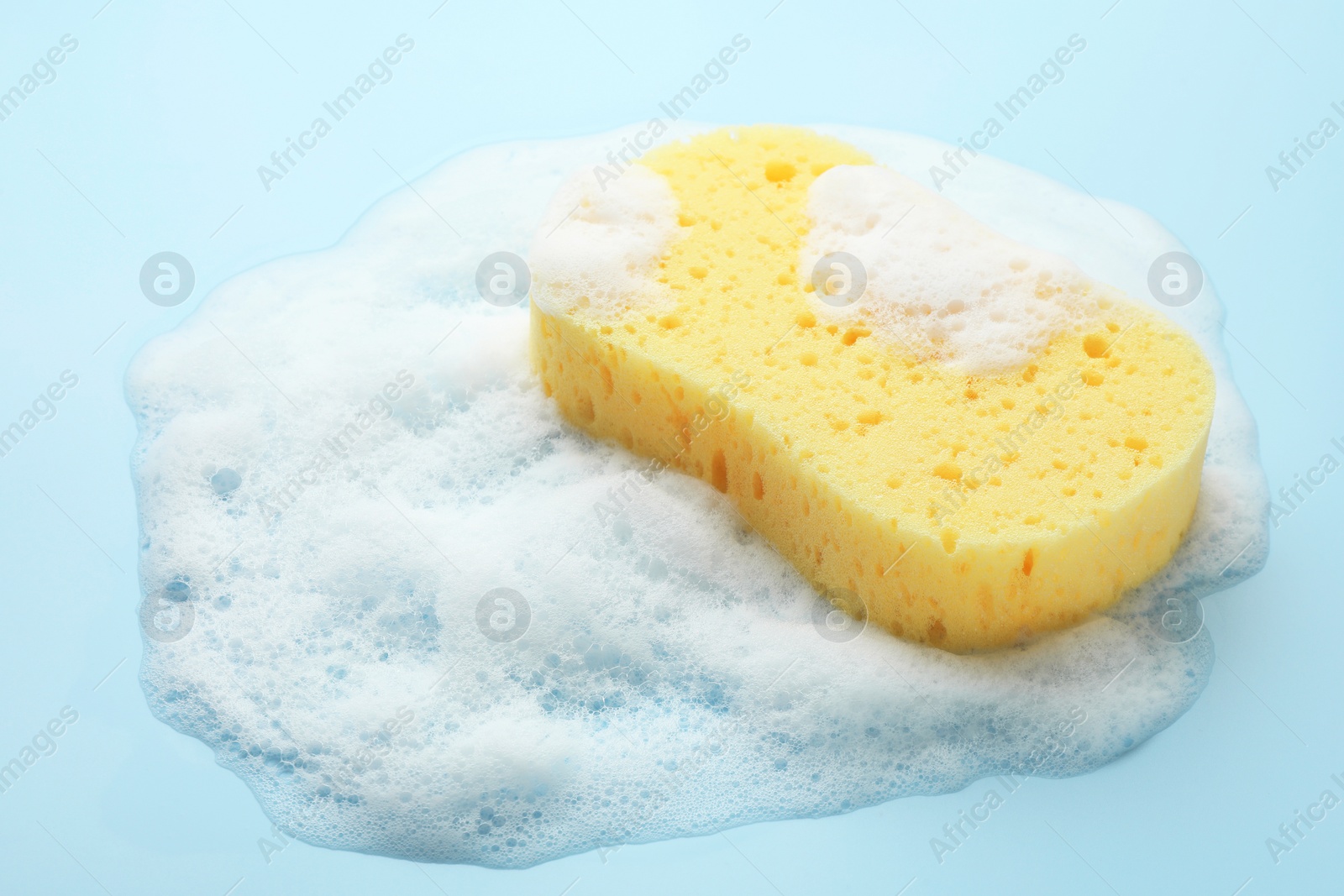 Photo of Yellow sponge with foam on light blue background