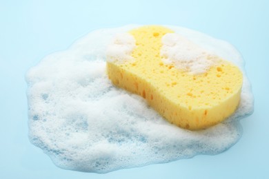 Photo of Yellow sponge with foam on light blue background