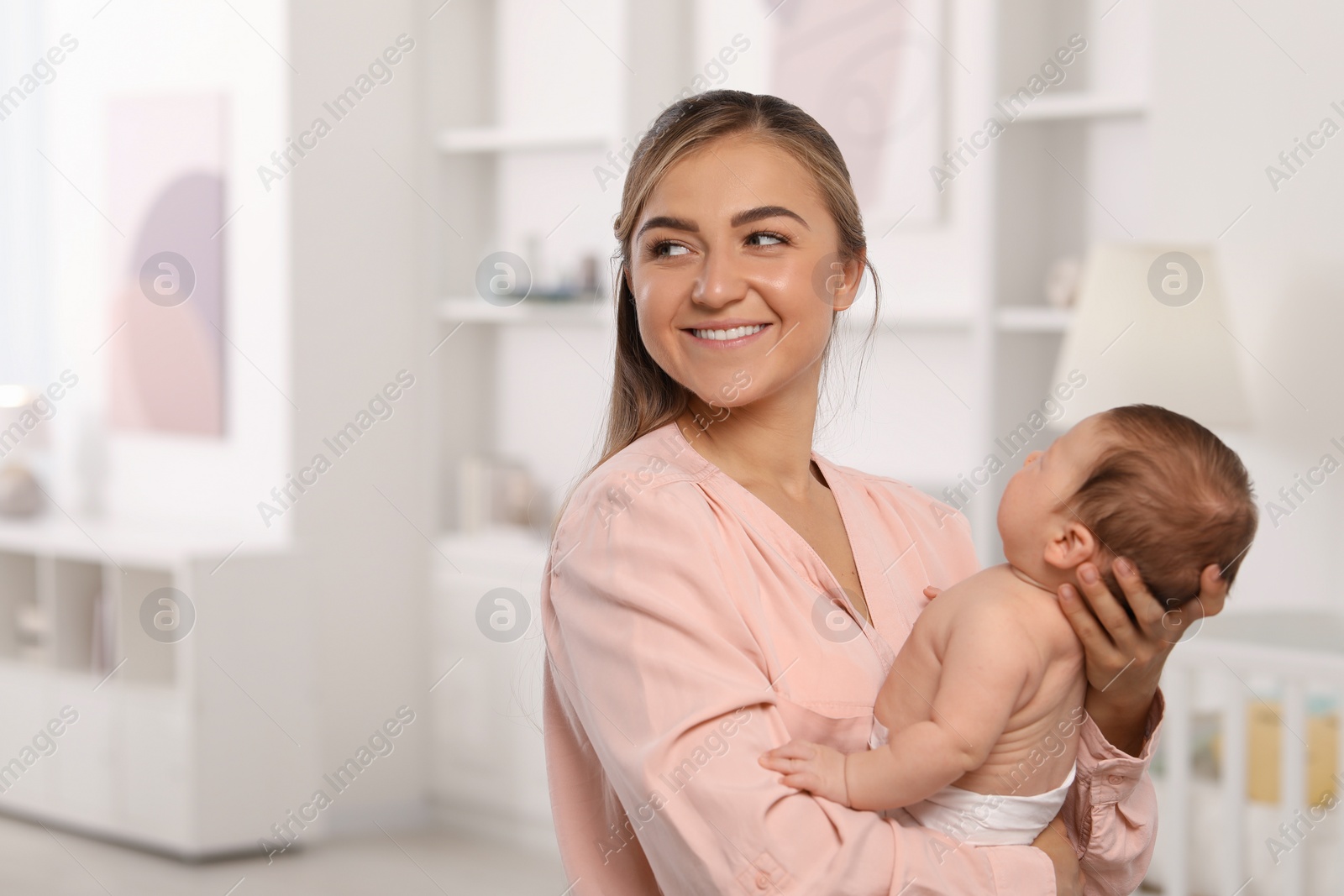 Photo of Mother holding her cute newborn baby in child's room, space for text