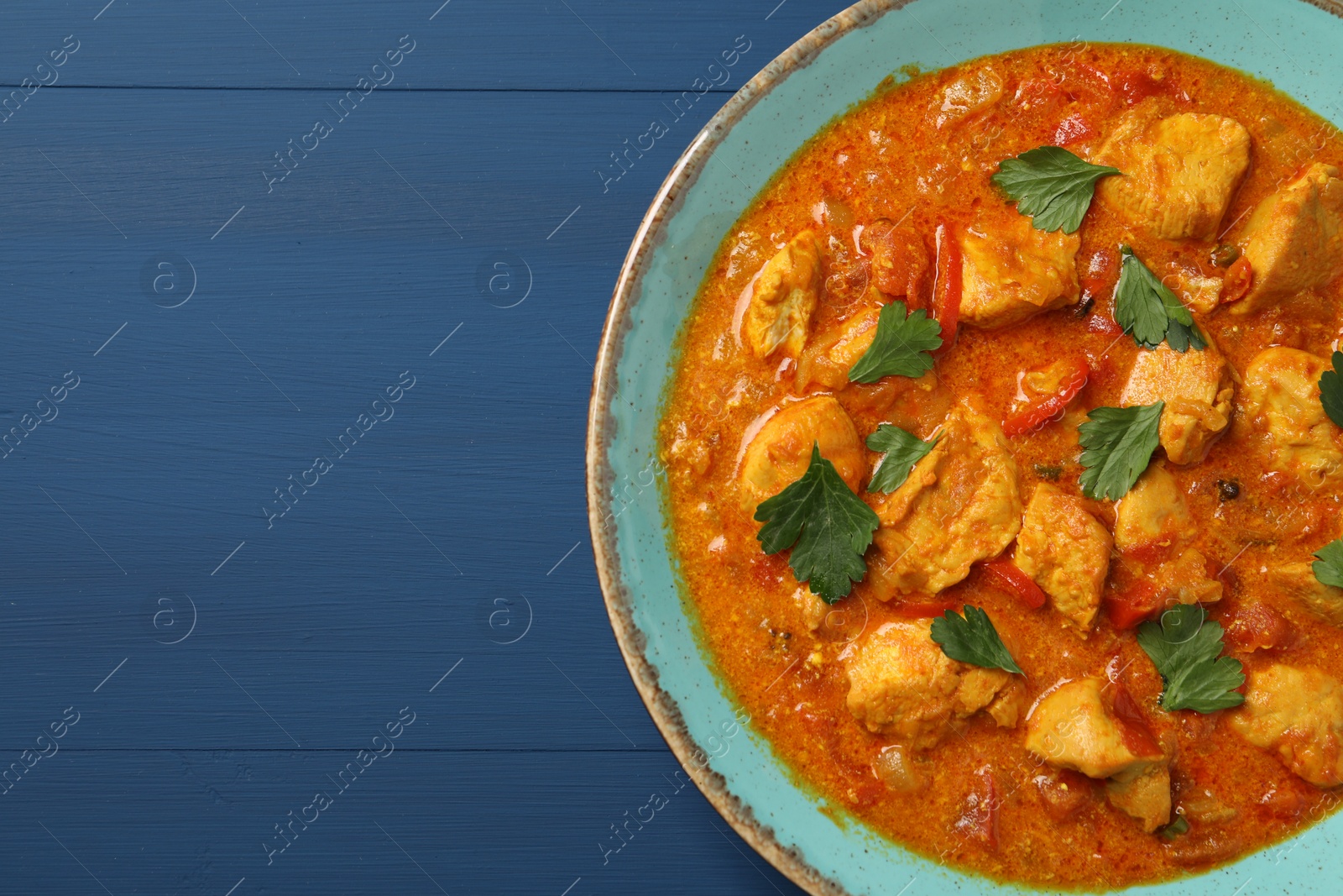 Photo of Delicious chicken curry on blue wooden table, top view. Space for text