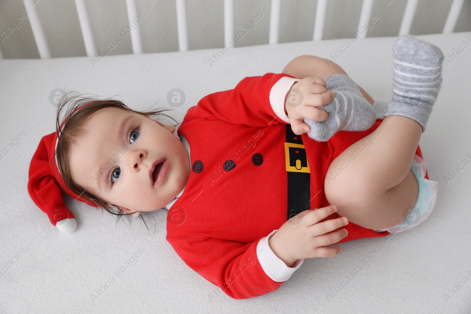 Photo of Cute baby wearing festive Christmas costume lying in crib, above view