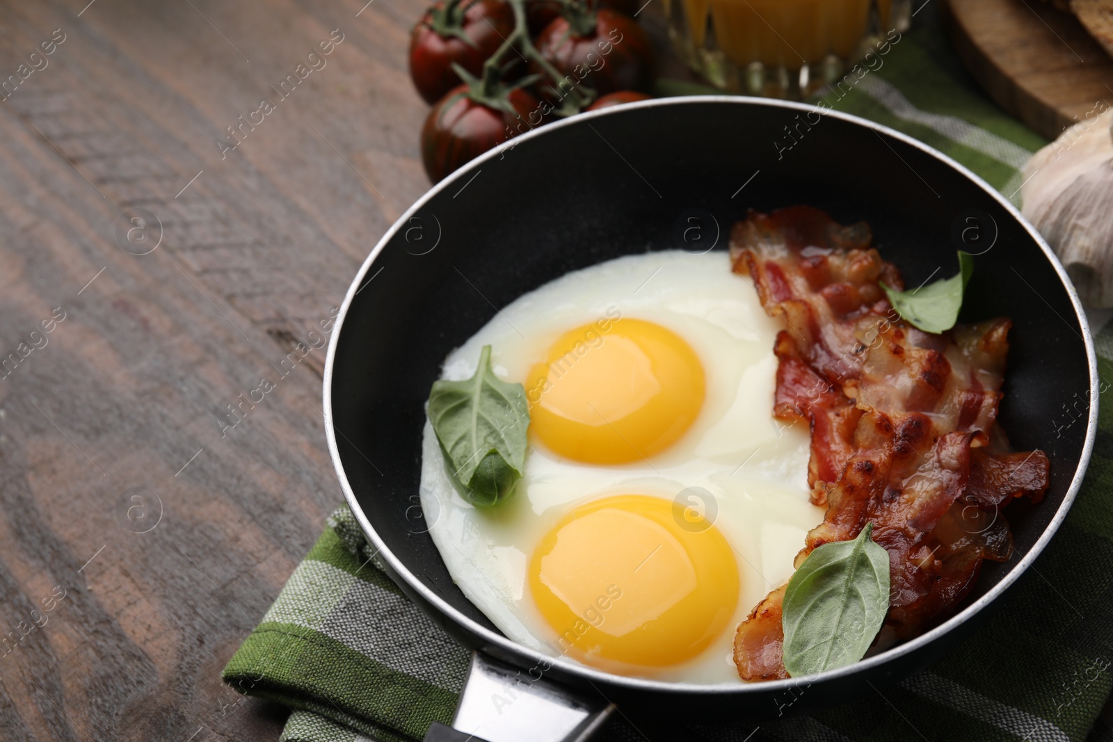 Photo of Fried eggs, bacon and basil in frying pan on wooden table