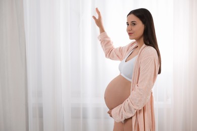 Beautiful pregnant woman in stylish comfortable underwear and robe indoors, space for text