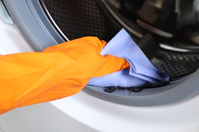 Photo of Worker cleaning empty washing machine with rag, closeup