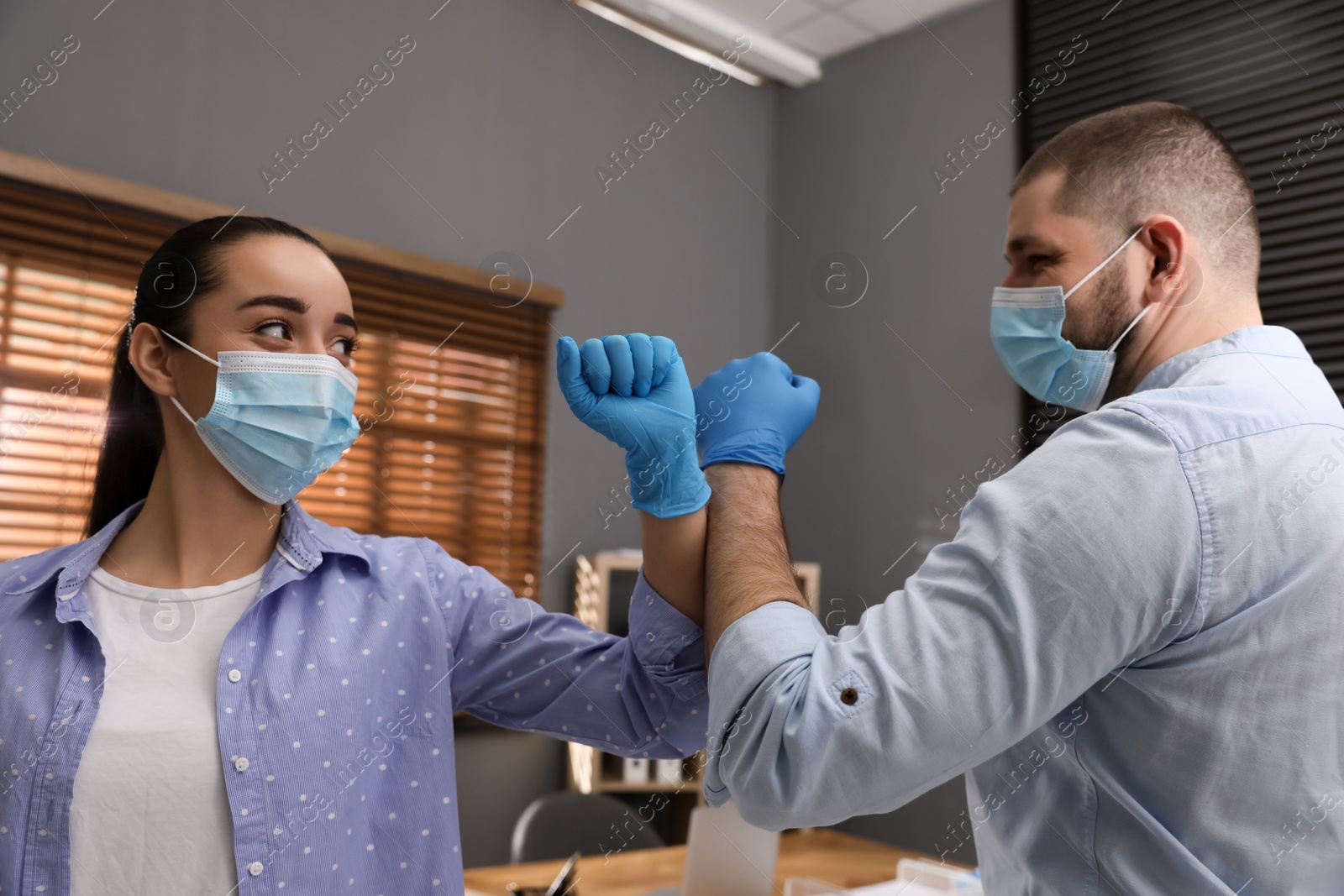 Photo of Office employees in masks greeting each other by bumping elbows at workplace