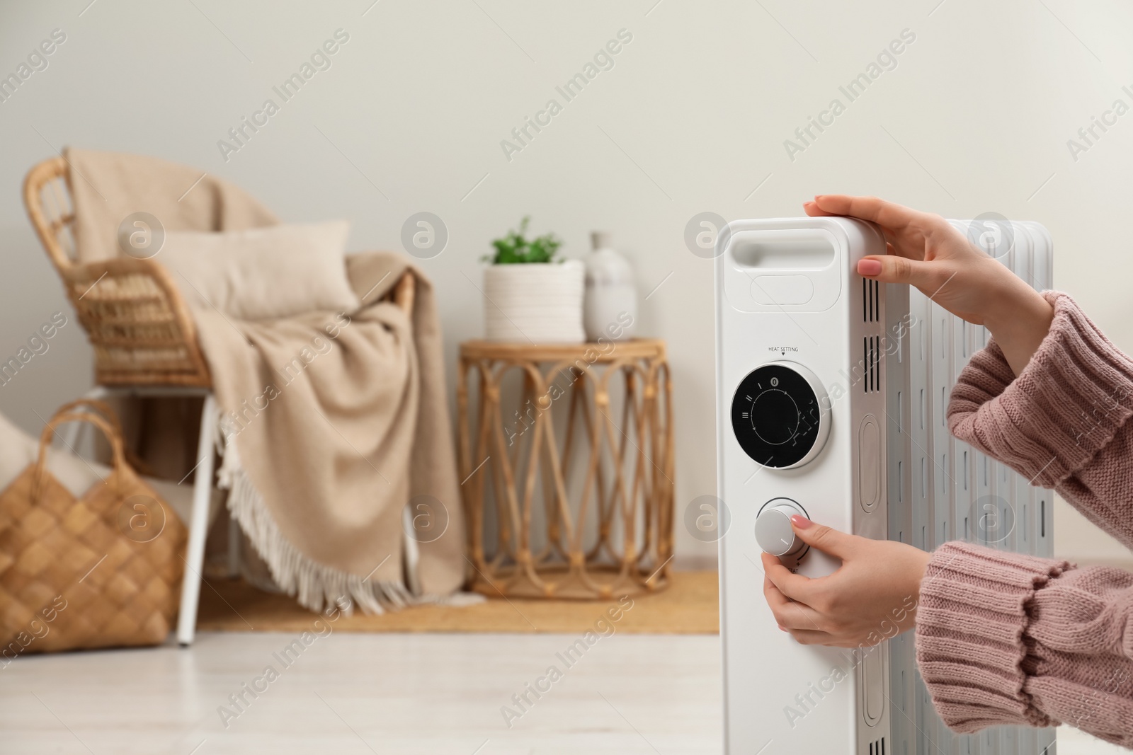 Photo of Woman adjusting temperature on modern portable electric heater indoors, closeup. Space for text