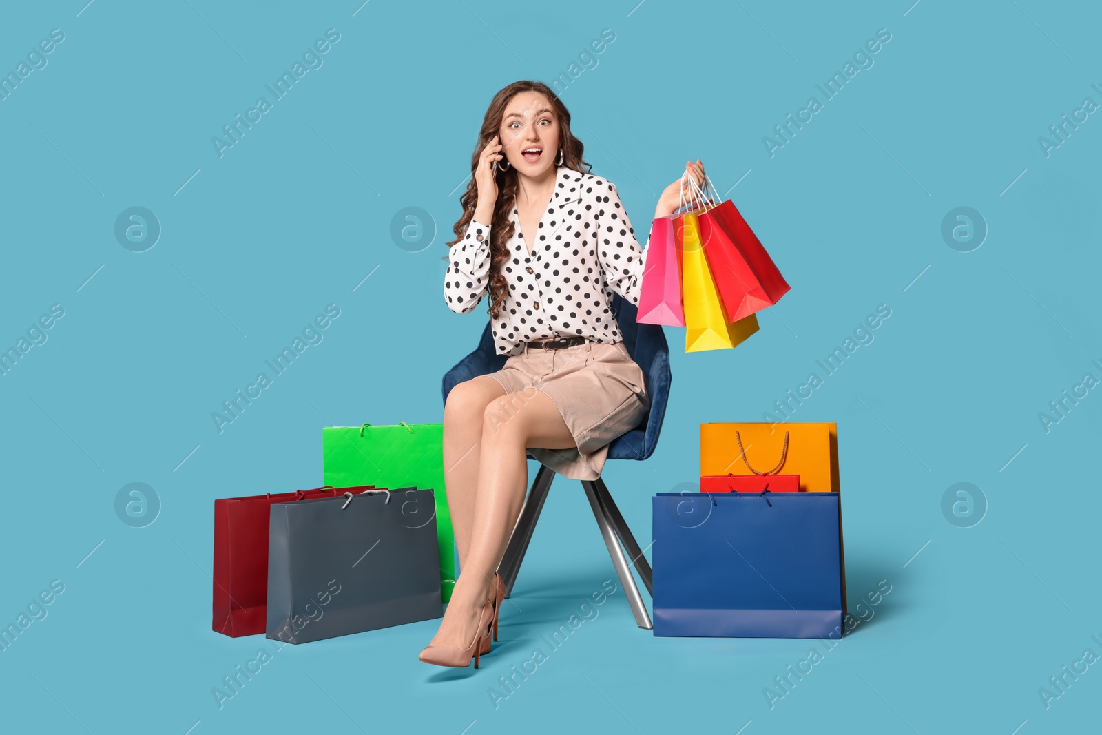 Photo of Excited woman holding colorful shopping bags on armchair against light blue background