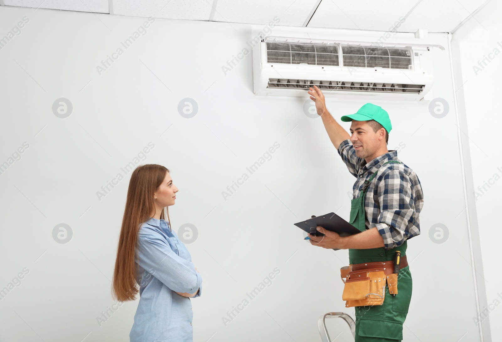 Photo of Male technician speaking with woman about air conditioner indoors