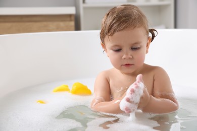 Photo of Cute little girl taking foamy bath at home