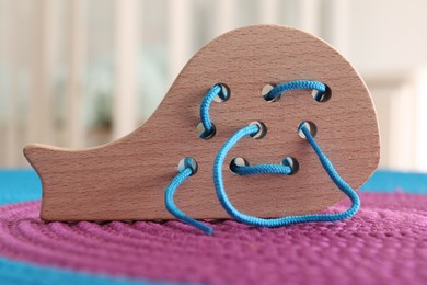 Photo of Motor skills development. Wooden lacing toy on color mat against light background, closeup