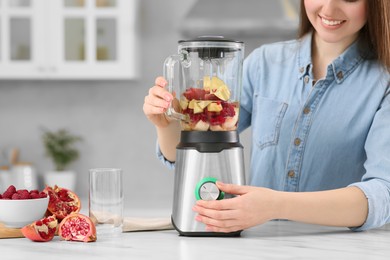 Photo of Beautiful young woman preparing tasty smoothie at white table in kitchen, closeup. Space for text