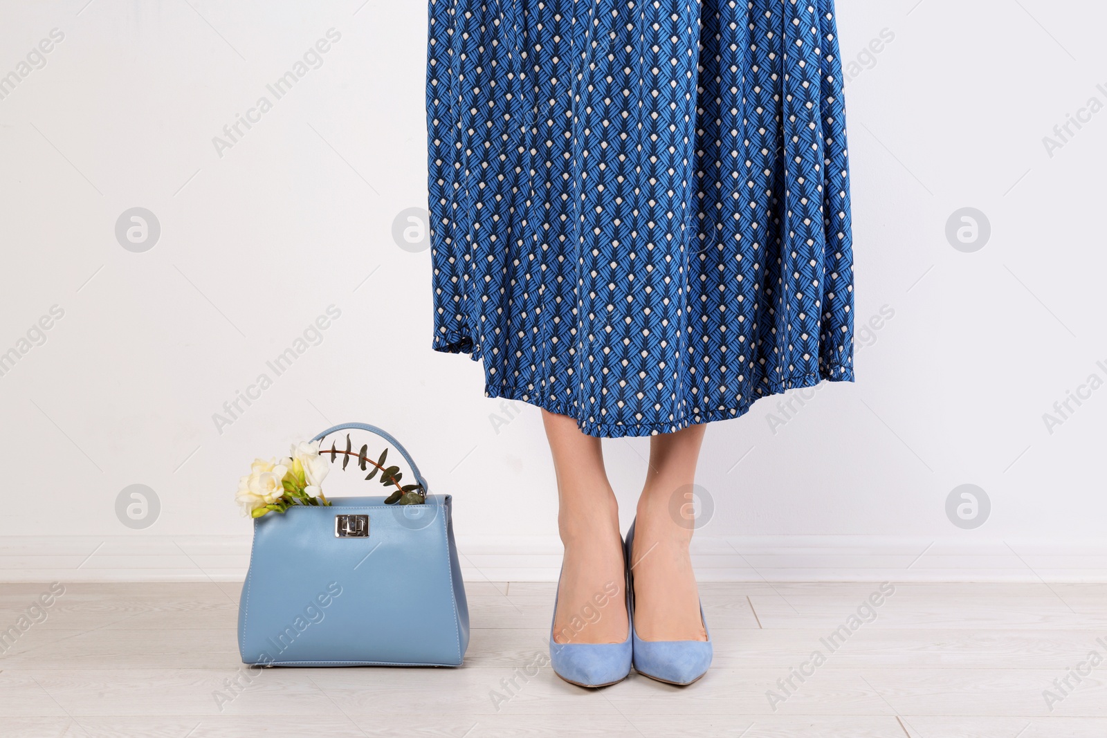 Photo of Stylish woman with handbag and spring flowers near light wall