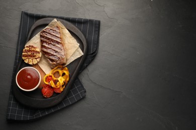 Delicious grilled beef steak with spices and tomato sauce on dark gray table, top view. Space for text