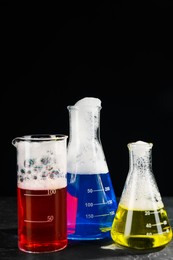 Photo of Laboratory glassware with colorful liquids on dark table against black background, space for text. Chemical reaction