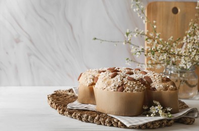Photo of Delicious Italian Easter dove cake (Colomba di Pasqua) and flowers on white wooden table. Space for text