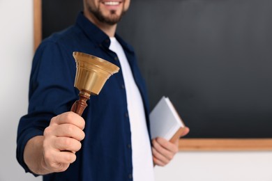Teacher with school bell near black chalkboard, closeup. Space for text
