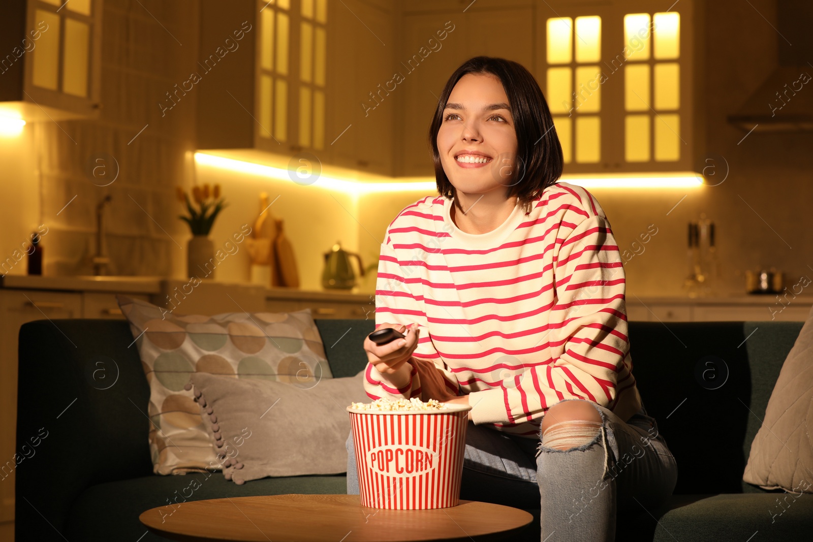 Photo of Happy woman watching TV with popcorn on sofa at home, space for text