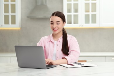 Woman using laptop at white table in kitchen
