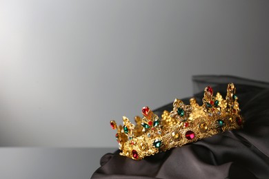 Photo of Beautiful golden crown with gems on dark cloth against grey background. Space for text