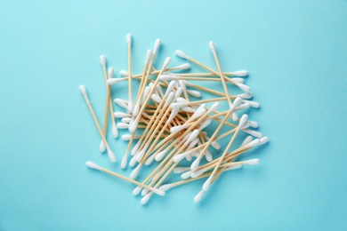 Photo of Heap of wooden cotton buds on turquoise background, flat lay