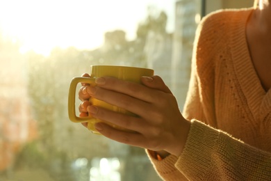 Photo of Woman holding cup with tea near window at home, closeup