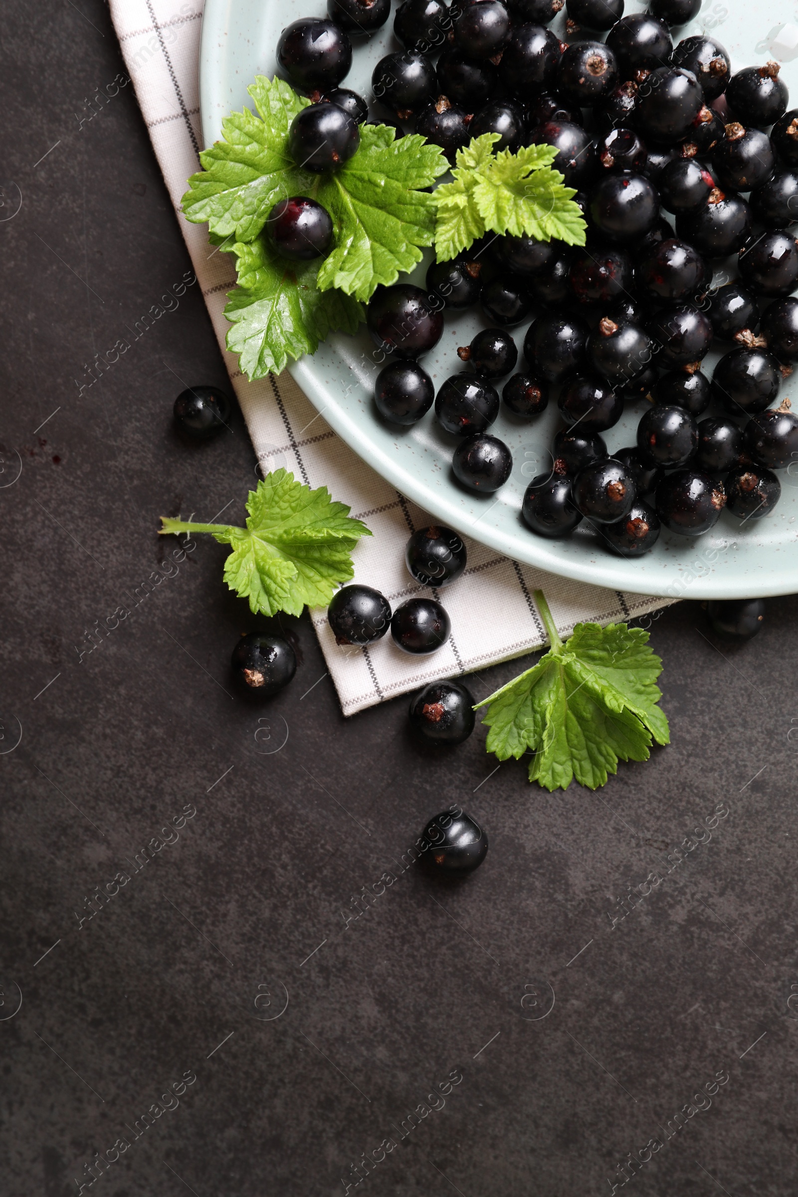 Photo of Plate with ripe blackcurrants and leaves on grey background, flat lay. Space for text