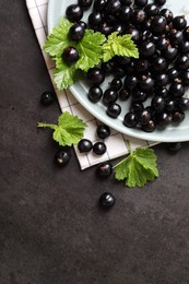 Plate with ripe blackcurrants and leaves on grey background, flat lay. Space for text