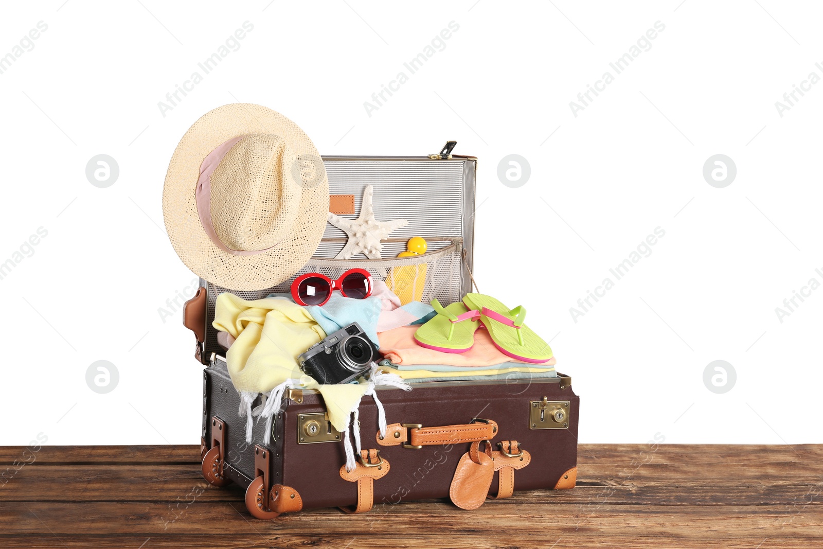 Photo of Open vintage suitcase with different beach objects packed for summer vacation on wooden table against white background