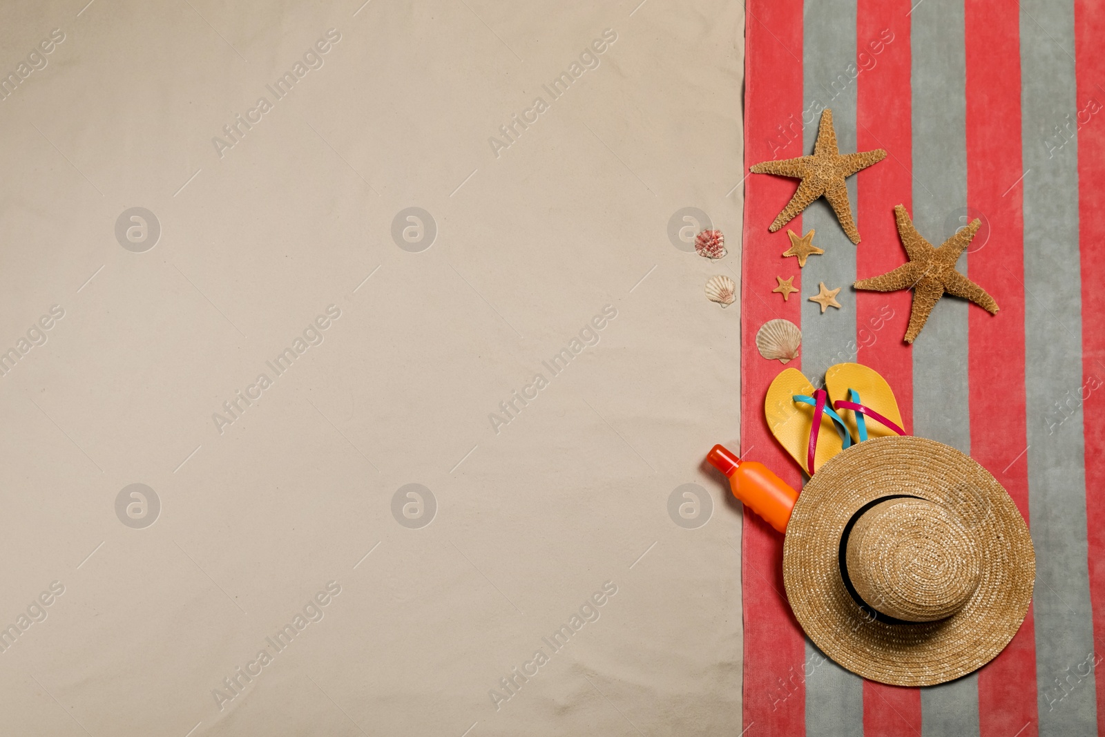 Photo of Beach towel, hat, sunscreen, starfishes, sea shells and flip flops on sand, flat lay