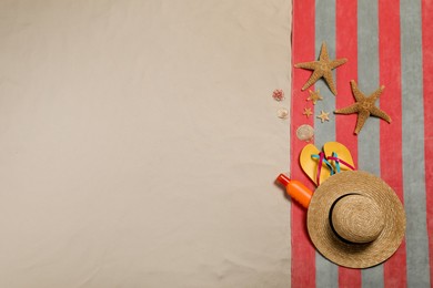 Photo of Beach towel, hat, sunscreen, starfishes, sea shells and flip flops on sand, flat lay